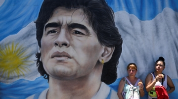 Members of social organizations stand next to a mural depicting late Argentine football star Diego Maradona during a protest at Pueyrredon bridge in Buenos Aires on December 2, 2022. (Photo by Luis ROBAYO / AFP)
