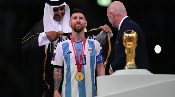 The Amir His Highness Sheikh Tamim bin Hamad Al Thani wraps the cloak around Lionel Messi as FIFA chief Gianni Infantino watches on: AFP/Paul Ellis