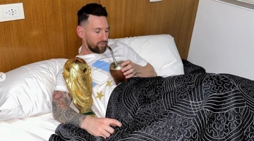 In this handout picture, Lionel Messi sips mate in bed while holding the FIFA World Cup Trophy at the AFA training centre in Ezeiza, Argentina, on December 20, 2022. (Photo by INSTAGRAM ACCOUNT OF @leomessi / AFP)