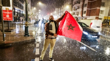 A Moroccan fan stands in the rain holding a national flag during the Qatar 2022 World Cup semi-final match between Morocco and France, in Rabat, on December 14, 2022. (Photo by FADEL SENNA / AFP)