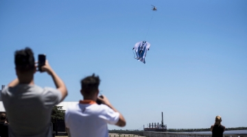 People take pictures with their cell phones of a helicopter carrying a giant t-shirt of Argentine forward Lionel Messi over Rosario, Argentina, on December 13, 2022. (Photo by AFP)